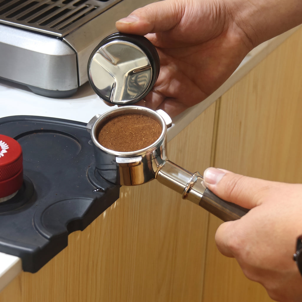 Dosing ground coffee into the 54mm portafilter on a kitchen counter
