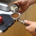 Dosing ground coffee into the 54mm portafilter on a kitchen counter
