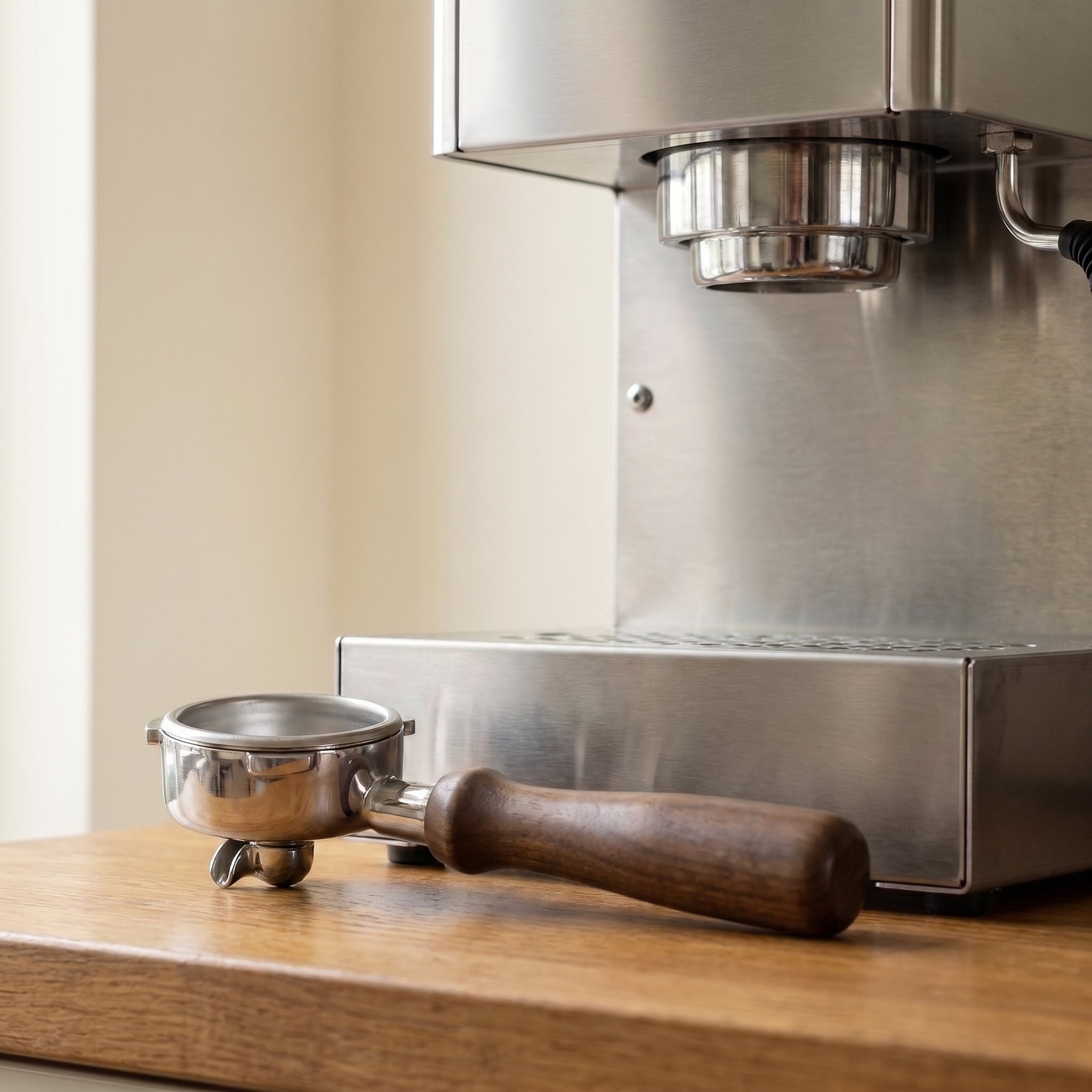 The 54mm bottomless portafilter resting on a kitchen counter beside a home espresso machine, showing its real size